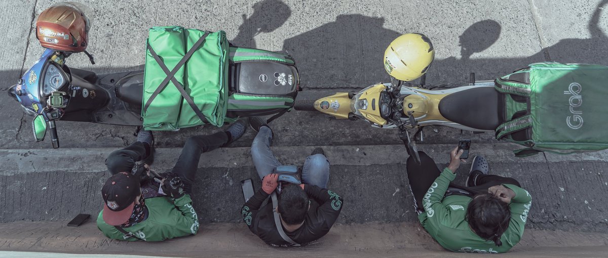Fahrer des Dienstleistungsunternehmens Grab warten im Schatten eines Gebäudes in Metro-Manila auf ihren nächsten Einsatz. Digitale Geschäftsmodelle für den Transport von Waren und Personen auf Knopfdruck, wie bei Grab, sind in vielen südostasiatischen Städten fester Bestandteil des Alltags geworden. (Foto: Jason Miraples on Unsplash)